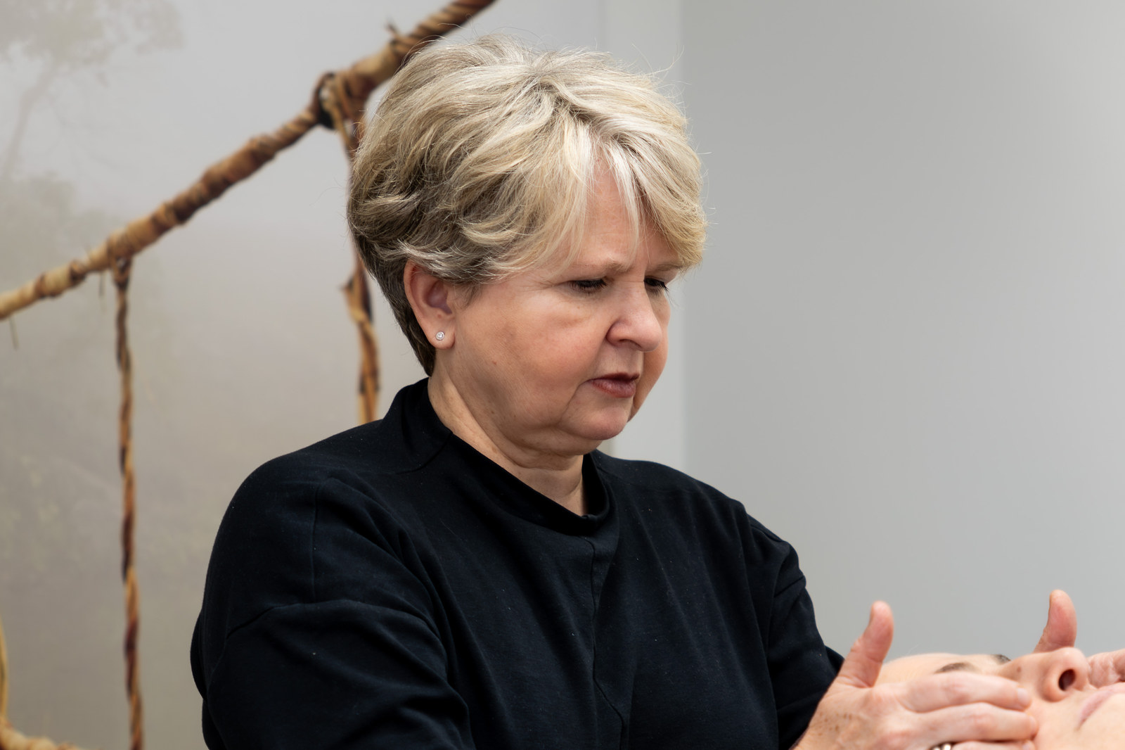 Karin, Physiotherapeutin, in konzentrierter HWS-Behandlung. Fokus auf die Hände, ruhige Arbeitshaltung.