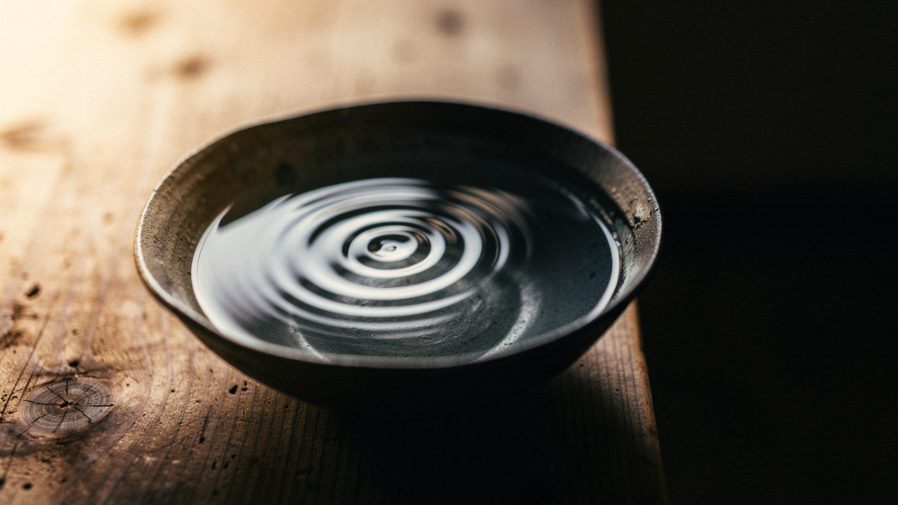 Konzentrische Wellenkreise auf stillem Wasser in einer flachen Keramikschale, warmes Seitenlicht (KI-generiert)